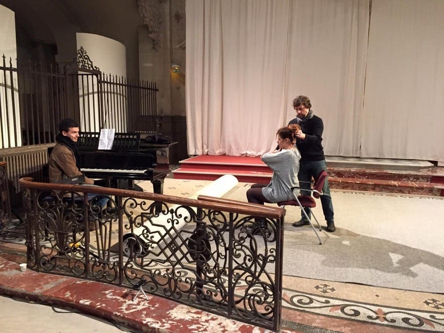 Robert Sussuma teaching a singing student by adjusting their neck posture by a piano on stage